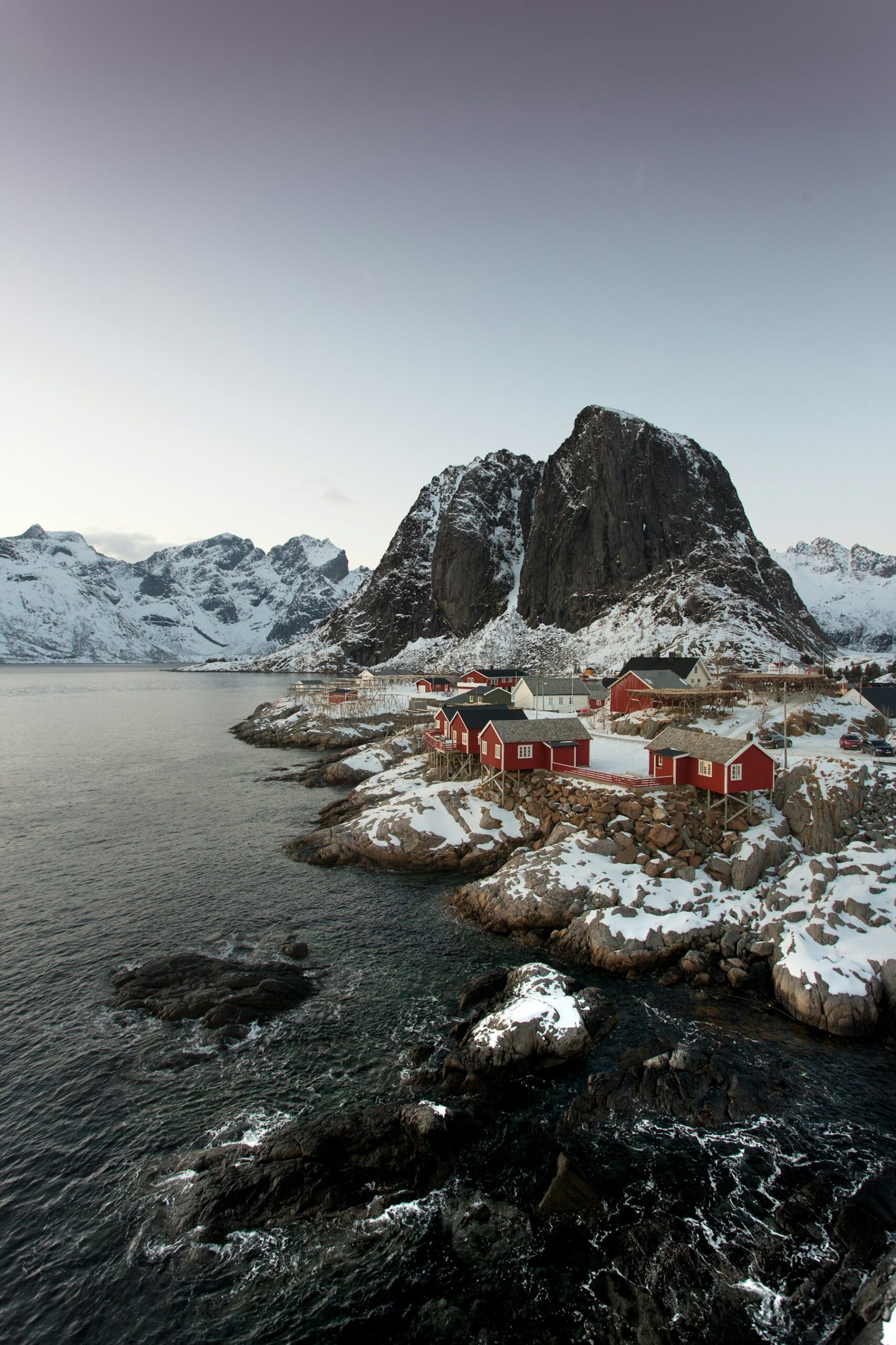 Rote Häuser am Wasser und verschneite Berge in Reine auf den Lofoten
