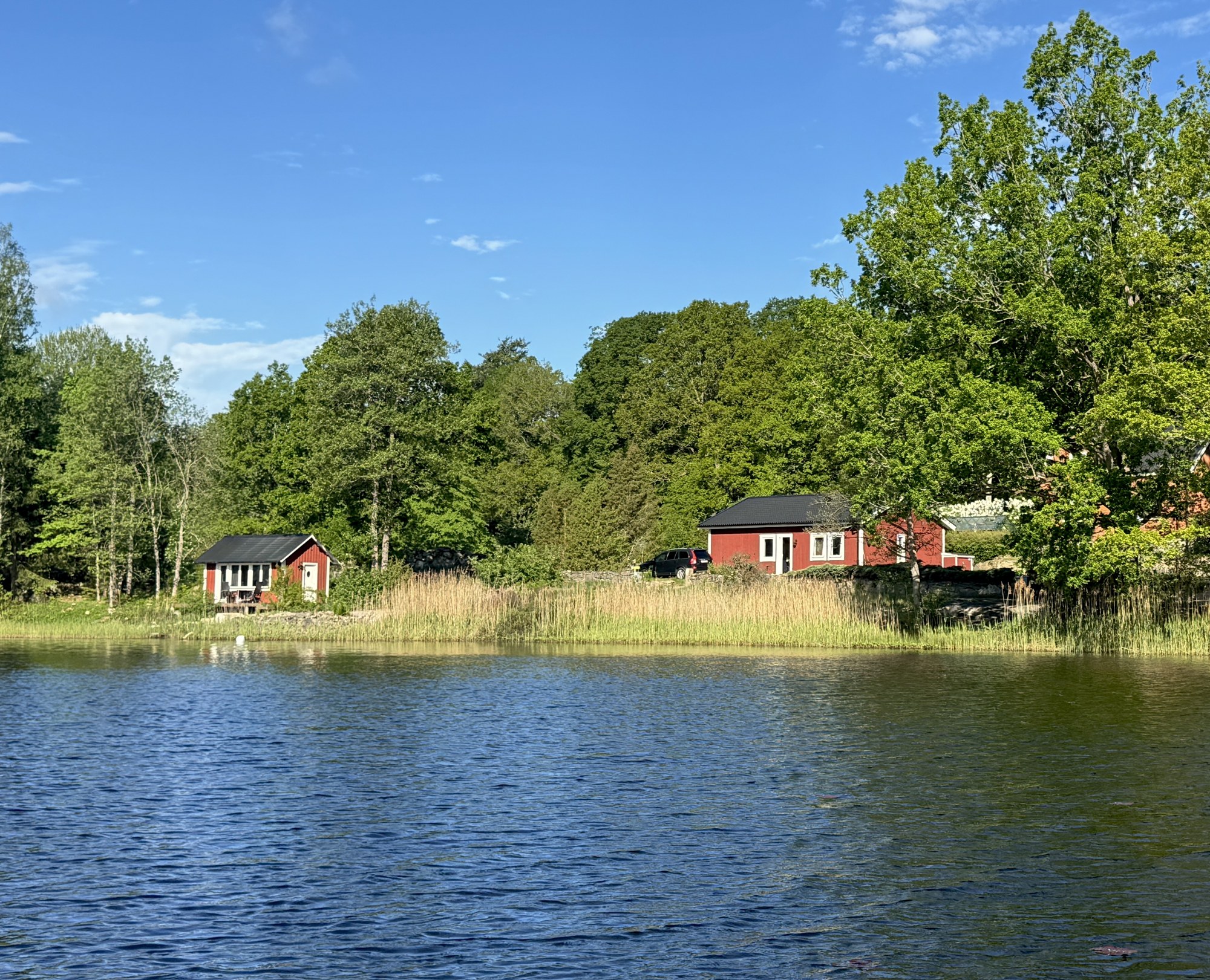 Rote Ferienhäuser am Ufer eines Sees in Södra Rågeboda, vom Wasser aus gesehen