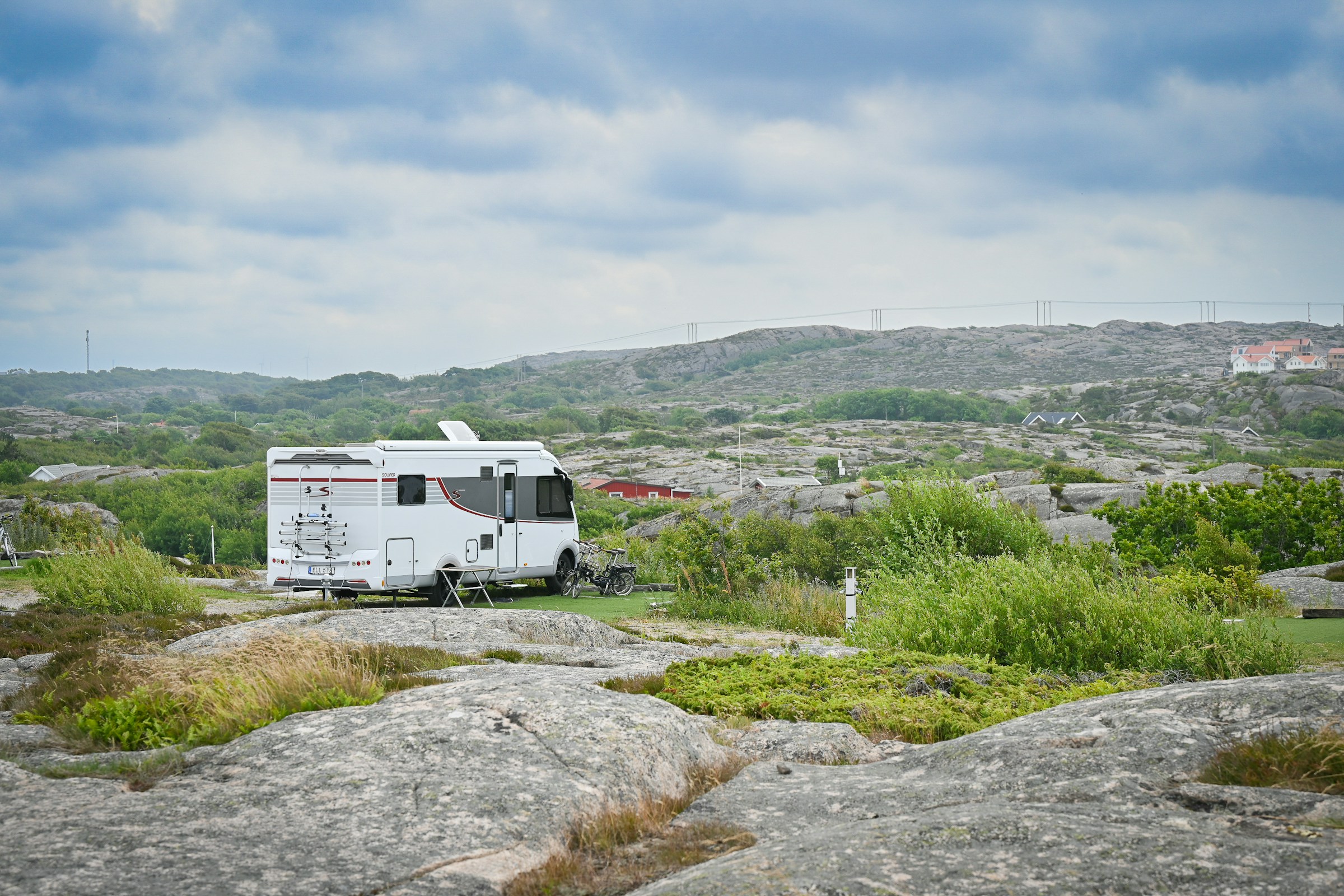 Klassisches weißes Wohnmobil zwischen Felsen und grüner Küstenvegetation in Schweden